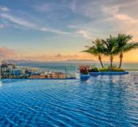Apartment construction in Pattaya with sea views, a swimming pool, and palm trees on the terrace.
