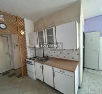 A kitchen in a studio apartment with a gas stove and cabinets, on a white wall.