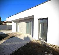 A family house in Turany with a light facade, featuring modern window elements on a paved courtyard.