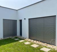 A family house in Turna with a white facade, shutters, and a manicured lawn.