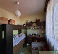 A room in a family house with a bed, table, and shelf.