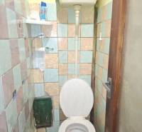 A simple bathroom in a family house with an older toilet and tiles.
