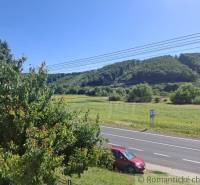 View from a family house in Lovinobaňa, road with a car, trees, and hills in the background.