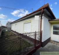 A family house in Nové Zámky with a garden behind a metal fence under a blue sky.