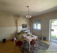 Interior of a family house with older furniture, a kitchen table, and open doors to the garden.