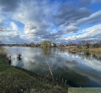 Idyllic landscape with a lake, clouds, and family houses in the background by the shore.