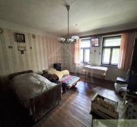 A room in a family house with a bed, wooden floor, and patterned wallpaper.