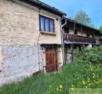 A family house in Pohorelá, stone walls, wooden balcony, surrounded by greenery and flowers.