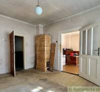 A room with a tiled stove, wooden floor, and kitchen in a family house.