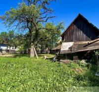 A garden in Gemerská Poloma by a family house, with a wooden structure and a large tree.