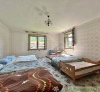 A bedroom in a family house with multiple beds, wallpapers, and windows with a view.