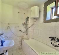A simple bathroom in a family house with a bathtub and a boiler on the wall.
