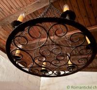 A wrought iron lamp with candles in the interior of a family house with a wooden ceiling.