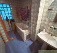 A bathroom with a dark bathtub, sink, and colorful stained glass window in a family house.