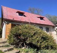 A cottage in Rožňava with a red roof, surrounded by lush greenery and a clear sky.