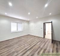 A room with a wooden floor and a window in a family house, neutral tones, ceiling lights.