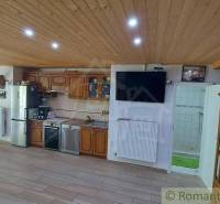 A kitchen in a family house with a wooden ceiling, kitchen unit, and a television on the wall.