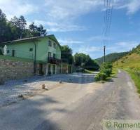 A family house in Dobrá Voda by the road surrounded by green hills and trees.