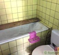 A bathroom in a family house with a bathtub and toilet, surrounded by yellow tiles.