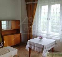 A room in a family house with a wooden dresser, a sofa, and a table by the window.
