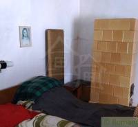 A room in a family house with a tiled stove, a bed, and wall pictures.