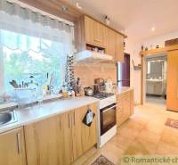 A kitchen in a family house with wooden cabinets, a stove, and a view through a large window.