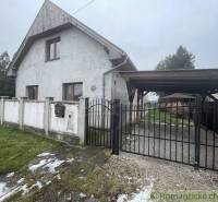 A family house with a white facade and gate, surrounded by a lawn and fencing.