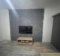 A television on a stone wall, with a wooden table underneath, in a room in a family house.