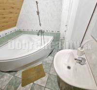 A bathroom in a family house with a sloped roof, a corner bathtub, and a sink.