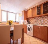 A kitchen in a 3-room apartment with a wooden cabinet, dining table, and washing machine.