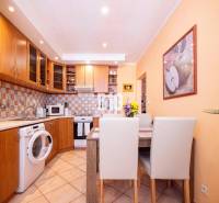 A kitchen in a 3-room apartment with wooden cabinets, a dining table, and a washing machine.