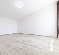 A spacious and bright room in a family house with white walls and parquet flooring.