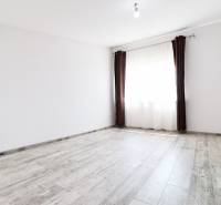 An empty room with white walls, brown curtains, and a wooden floor in a family house.