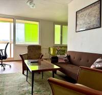 Living room in a three-room apartment with a brown couch, armchairs, and a desk.