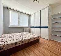 A room in a 3-room apartment with a bed, wardrobe, and shelves on the wall.