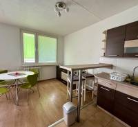 A kitchen in a 3-room apartment with a round table, green chairs, and a kitchen unit.