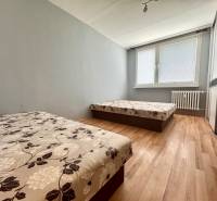 Two beds, wooden floor, and a window with blinds in a three-room apartment.