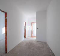 A hallway in a family house with white walls and an unfinished floor.