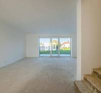 A space in a family house with large windows and a concrete floor, stairs in the background.