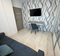 A room in a family house with wavy wallpaper, a television, a sofa, and a desk.