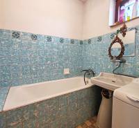 A bathroom in a family house with a bathtub, sink, and washing machine, tiled with blue tiles.