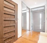 A hallway in a family house with a wooden floor, a mirror, and doors with geometric elements.