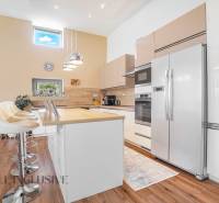 A kitchen in a family house with white cabinets, bar stools, and built-in appliances.
