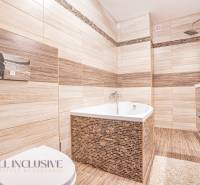 A bathroom in a family house with a bathtub, shower, and sink, surrounded by beige tiles.