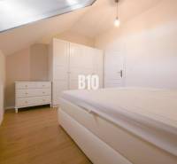 A bedroom in a 3-room apartment with a slanted ceiling, a white bed, and a wardrobe.