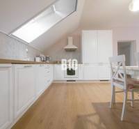 A bright kitchen in a 3-room apartment with white cabinets, wooden flooring, and a dining table.