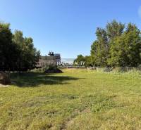 A green plot designated for residential living in Veľký Meder, surrounded by trees and grass.