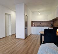 Kitchen and dining area in a 2-room apartment with wooden flooring and white furniture.