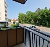 View from the balcony onto Sadová Street in Senica, overlooking the parking lot and greenery.