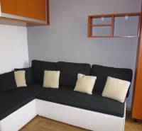 A sofa with cushions in a 3-room apartment, a wall with cabinets and a shelf.
